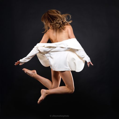 Γυναίκα μοντέλο σε άλμα με λευκό σακάκι, fashion φωτογράφιση σε μαύρο φόντο με φωτισμό Godox.